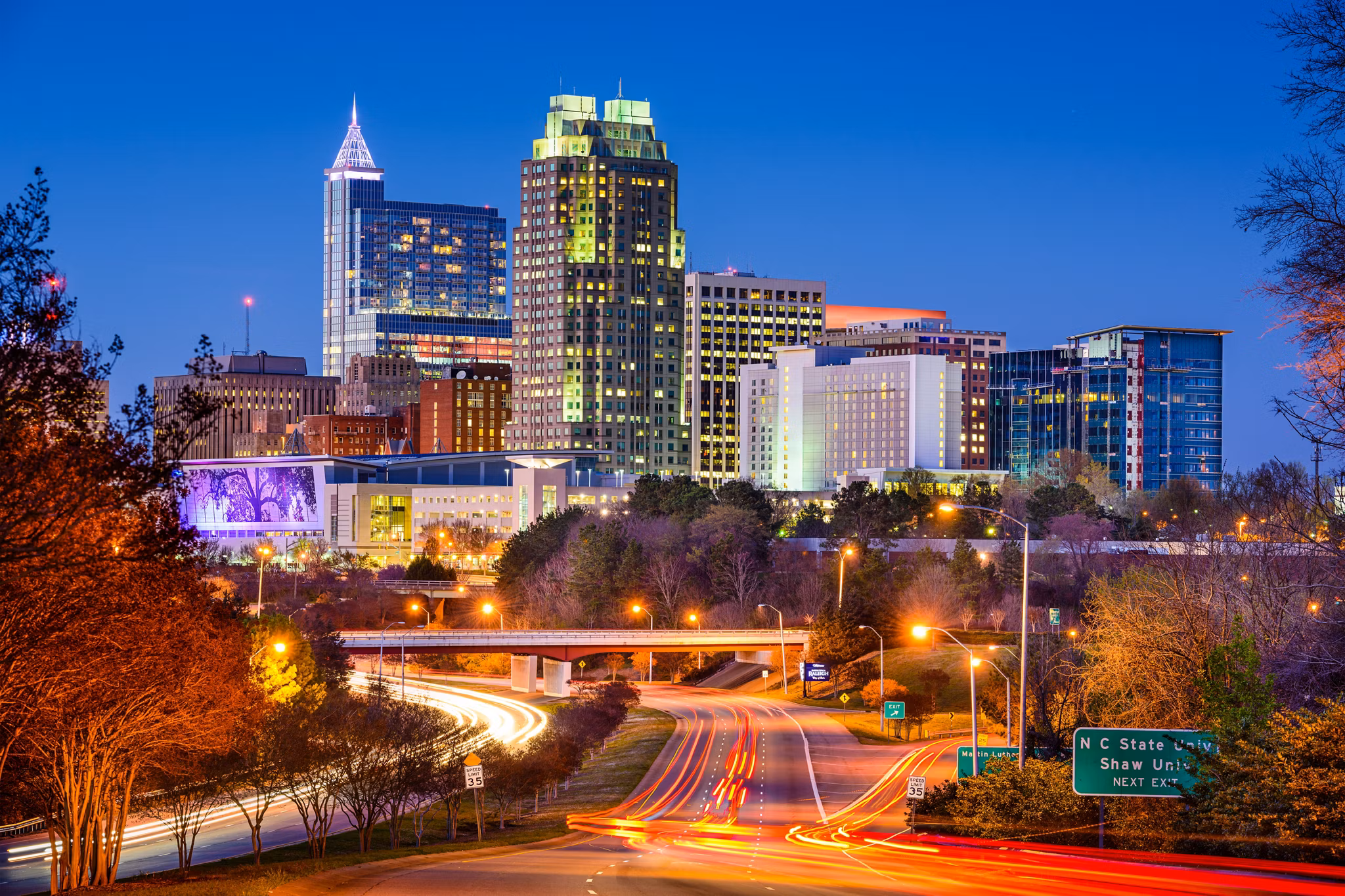 A beautiful panoramic photo of the downtown Raleigh cityscape and skyscrapers against a clear blue sky, this is Raleigh, North Carolina.