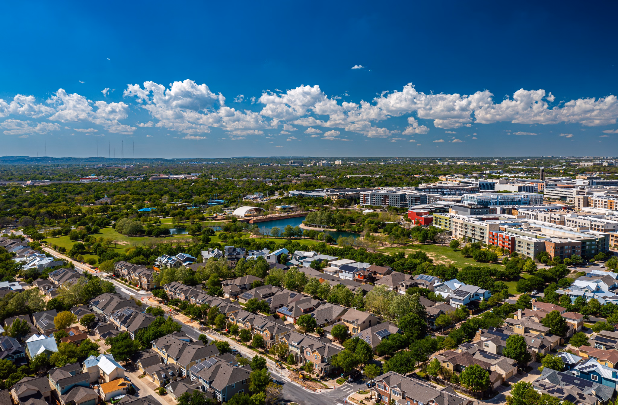 Aerial view of the Mueller/East MLK neighborhood in Texas, showing green parks, houses, and modern buildings under a blue sky.