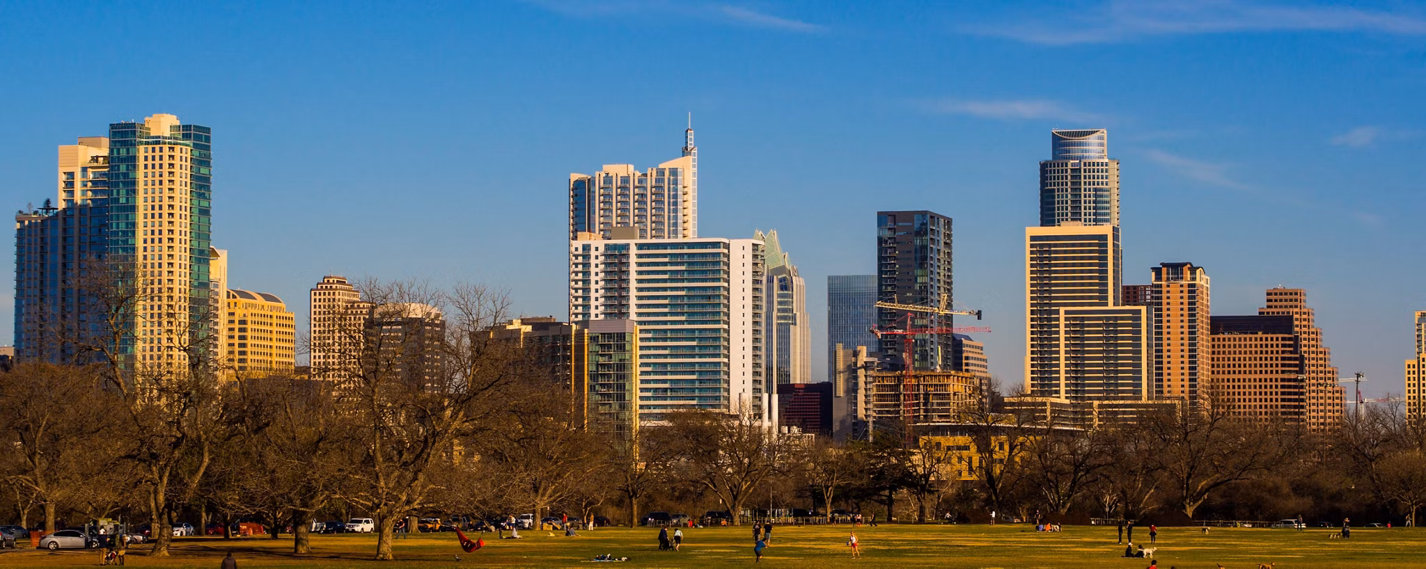 City skyline of modern buildings near Zilker/Bouldin Creek in Texas, with a park in the foreground and blue sky.