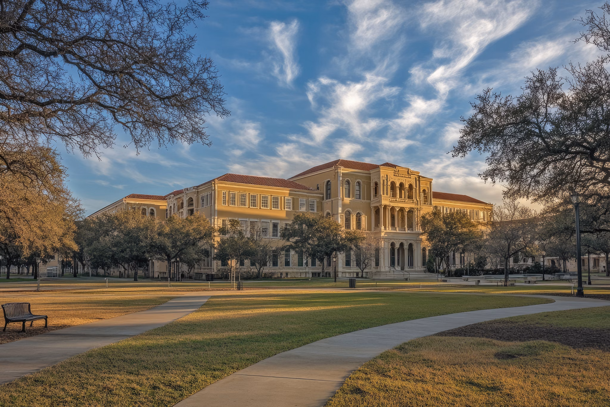 A historic building surrounded by trees and grass in College Station, Texas, under a partly cloudy sky.
