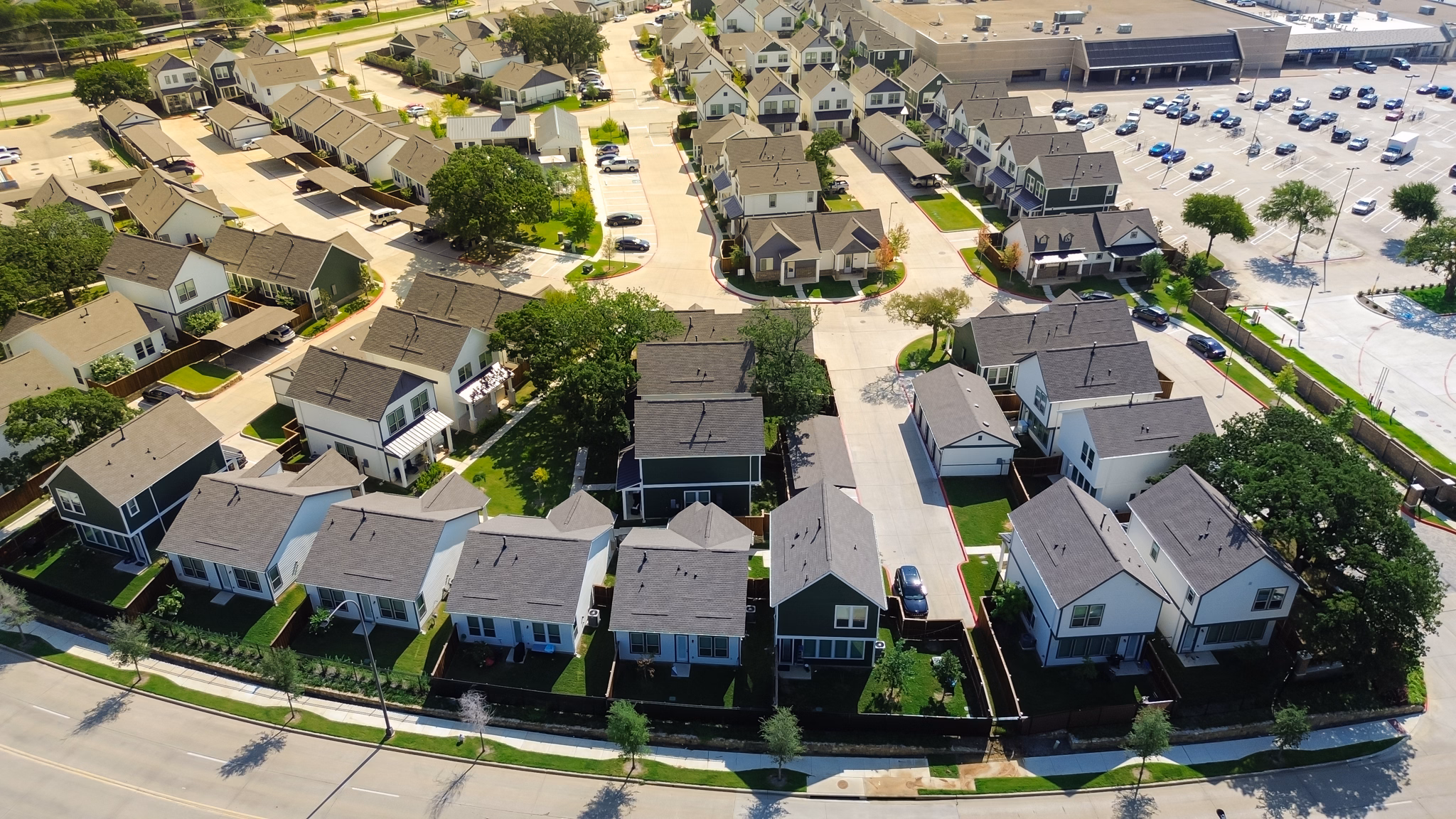 Aerial view of homes in Northeast Dallas, Texas, featuring green lawns and trees, with a shopping area in the background.