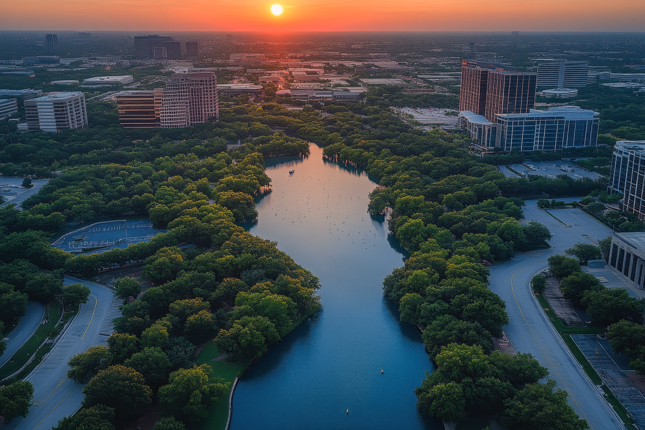 A scenic view of the Plano/Richardson area in Texas at sunset, featuring a river surrounded by trees and buildings.