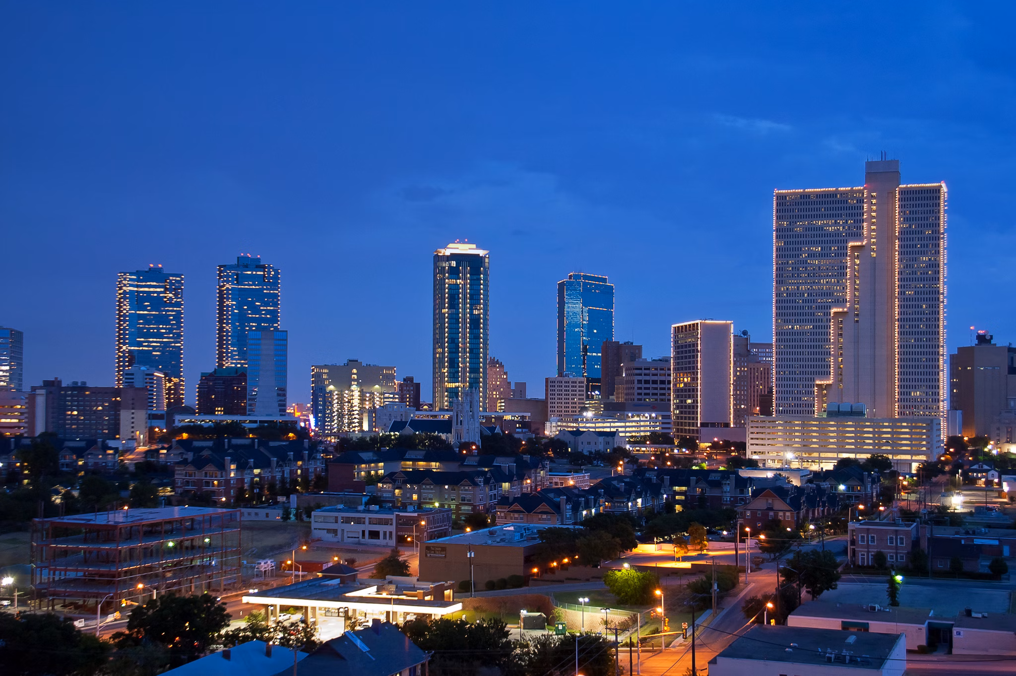 A skyline view of Fort Worth, Texas, at dusk, featuring brightly lit buildings against a darkening sky.
