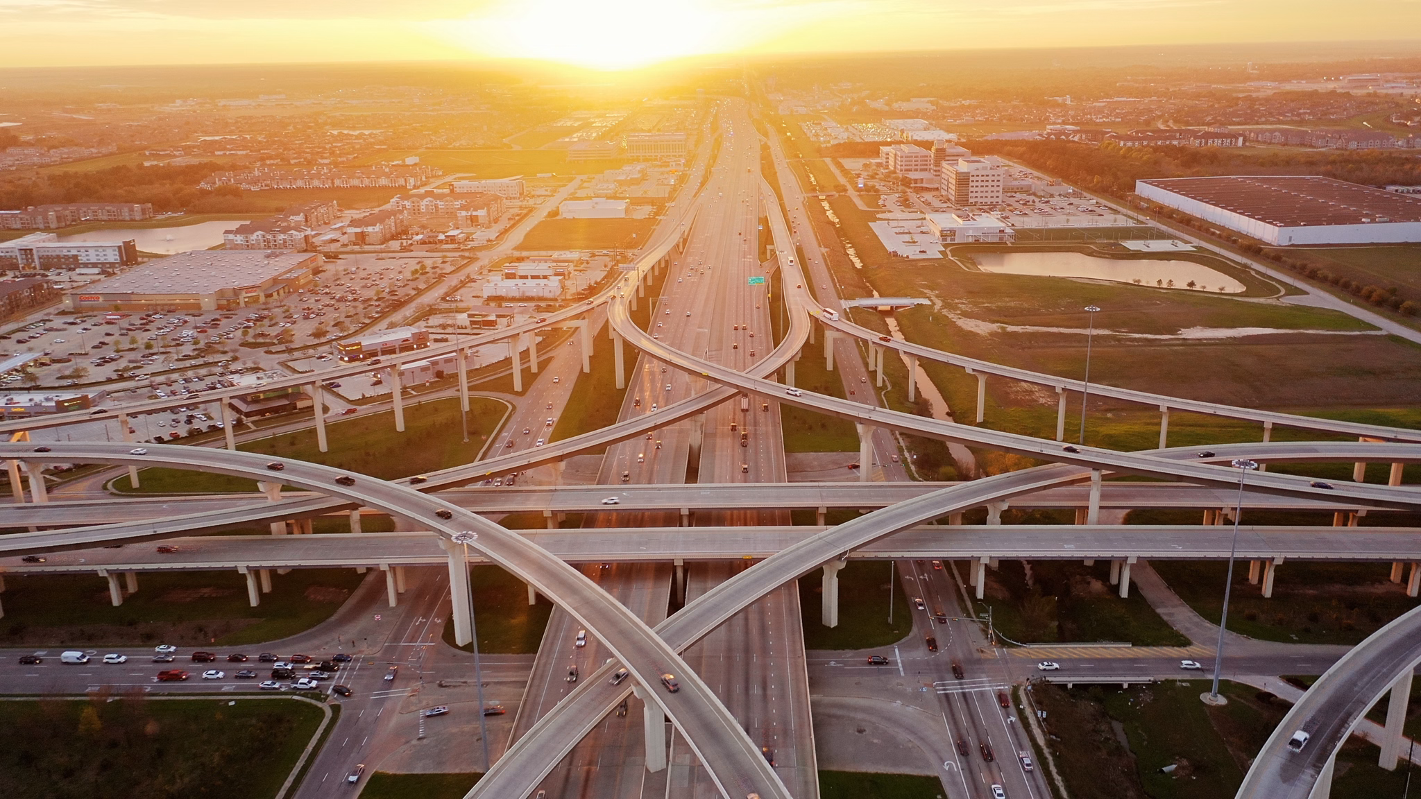 Aerial view of highways and roads in Katy, Texas, during sunset with buildings and greenery in the background.