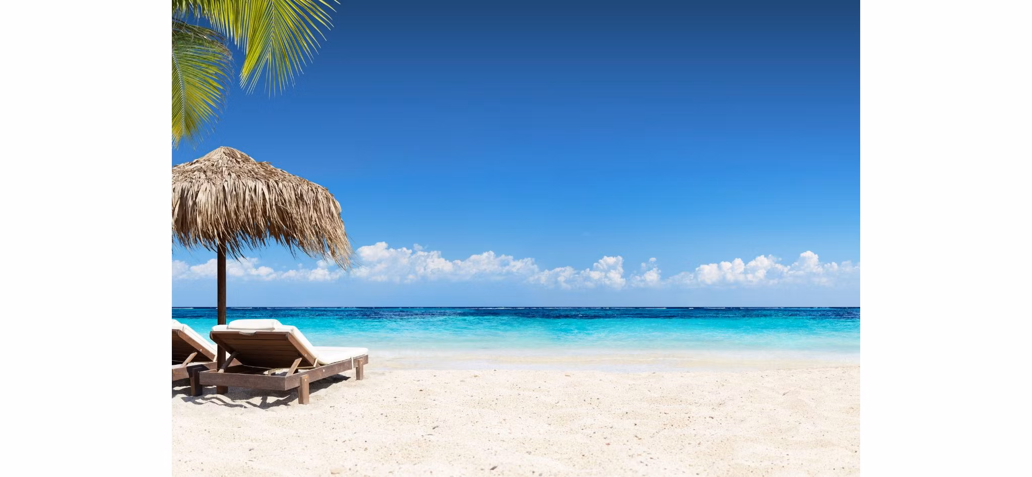 Tropical beach scene with clear blue sky, turquoise sea, white sand, a straw umbrella, and a pair of sun loungers.