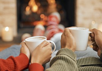 Two people enjoying warm drinks by the fireplace, showcasing a cozy and relaxing atmosphere with a blurred background, perfect for winter warmth.