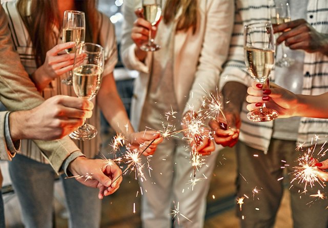 Group of people holding champagne glasses and sparklers, celebrating together.