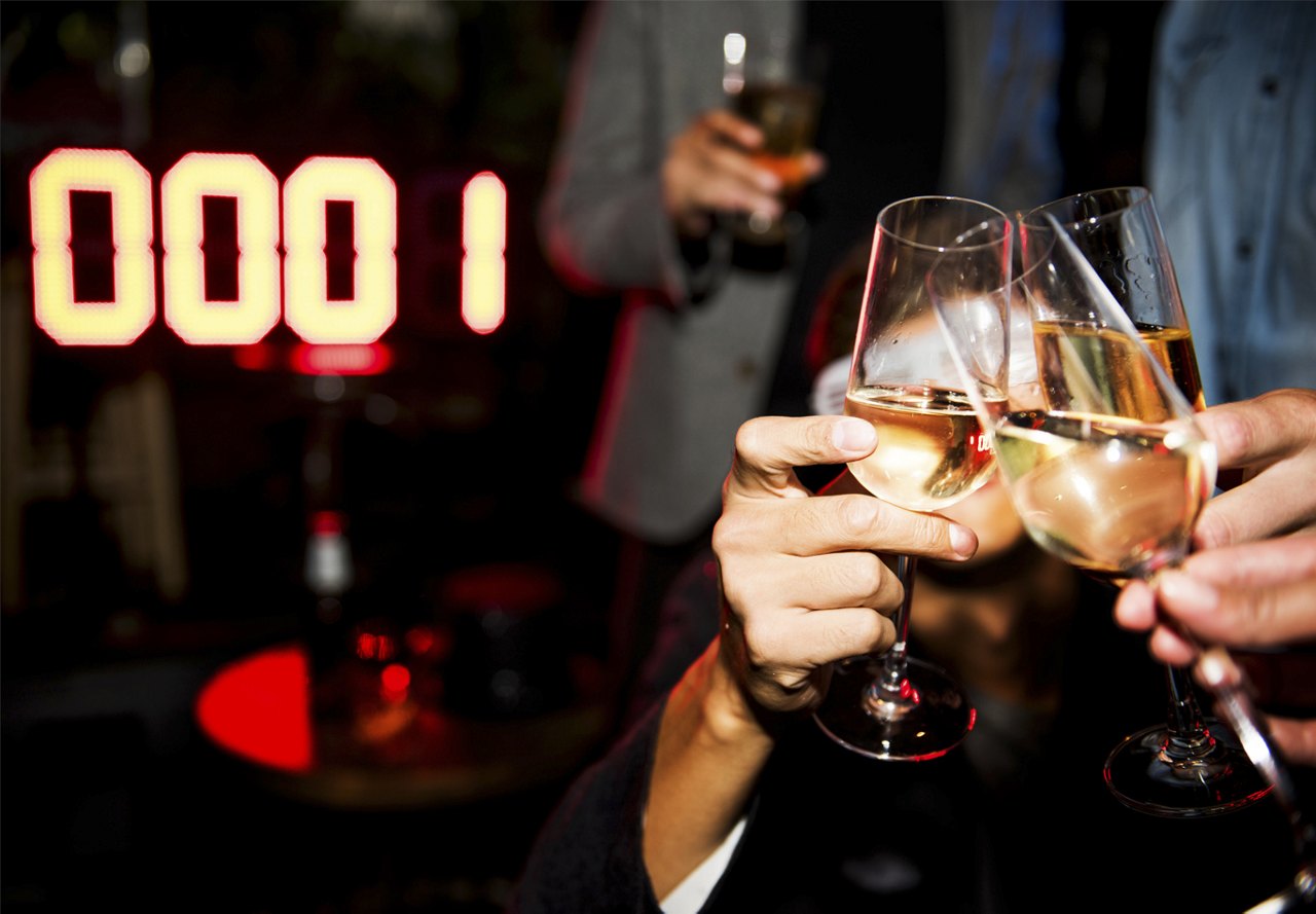 Close-up of a New Year's Eve toast with champagne glasses against the backdrop of a digital countdown display showing '0001'.