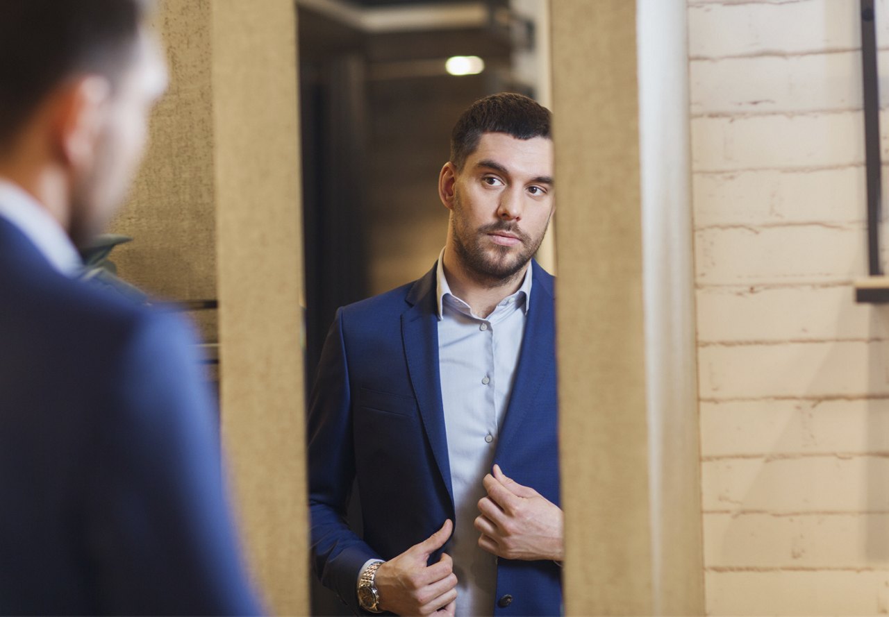 Confident man in a business suit adjusting his jacket while looking in the mirror.