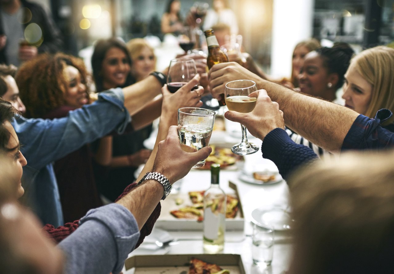 A group of friends toasting with drinks over a dinner table, celebrating a special occasion.