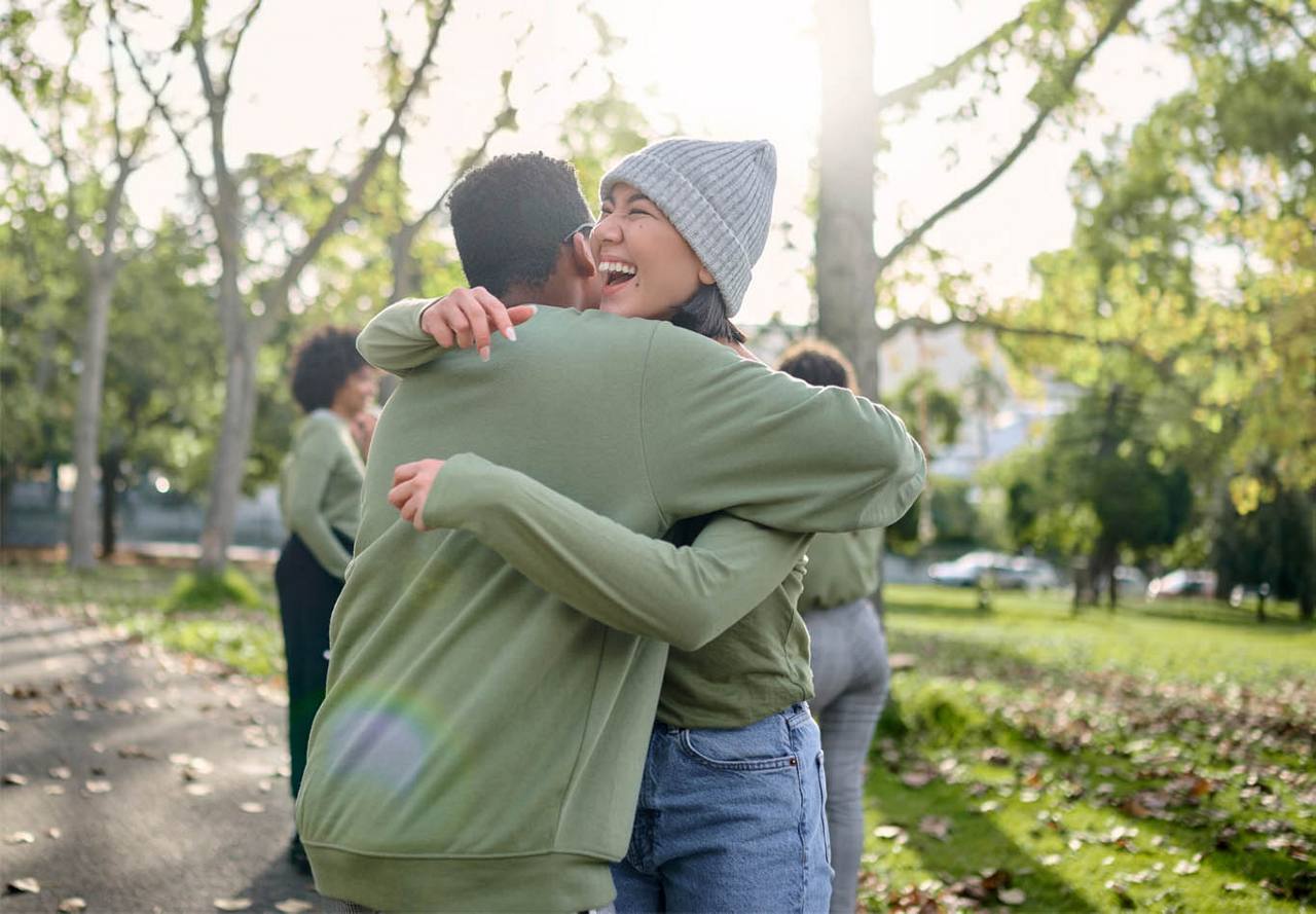 A joyful woman embracing a man in a park with autumn leaves on the ground and a lens flare effect from the sun.