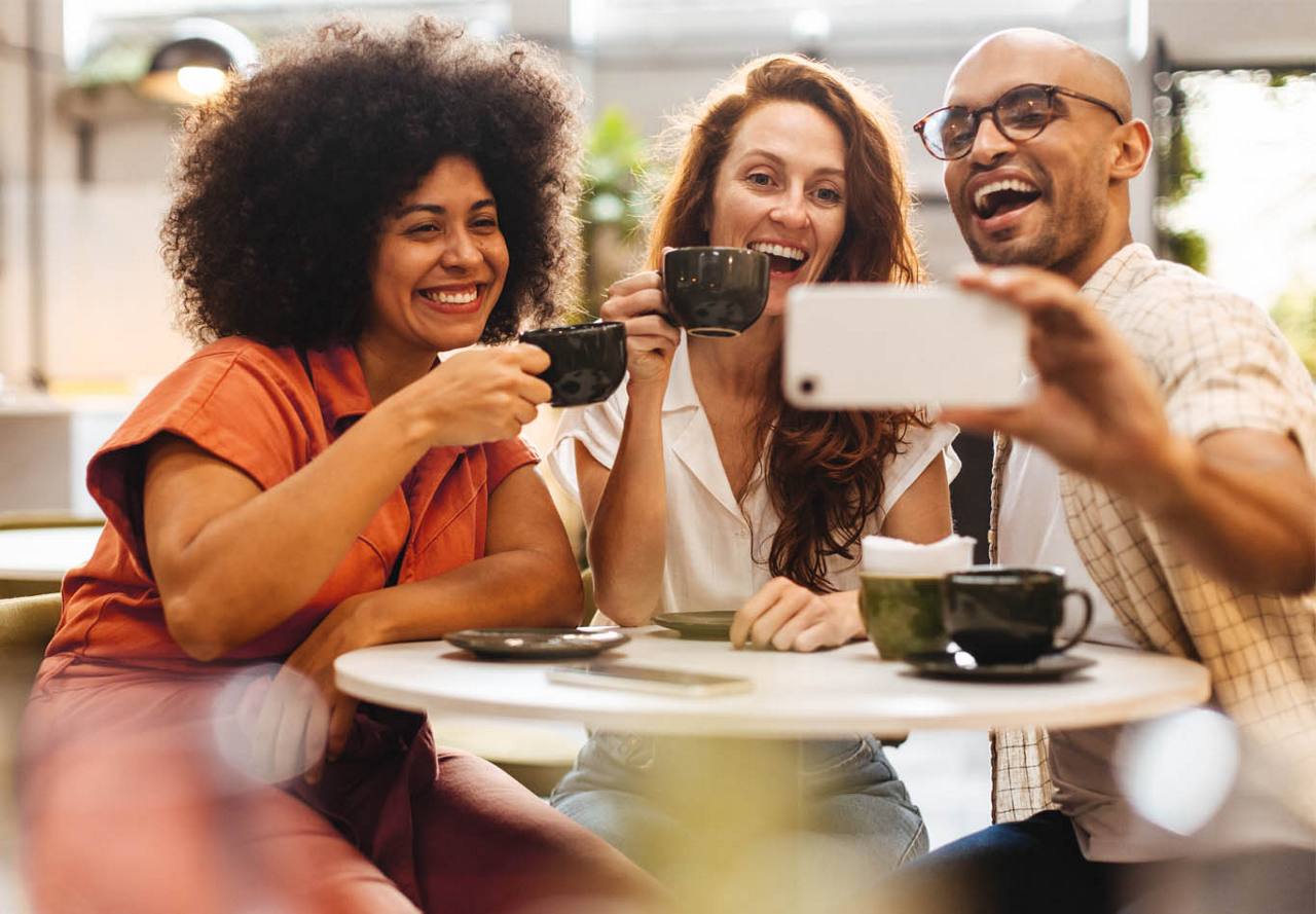 Three friends enjoying coffee and taking a selfie together at a cafe.