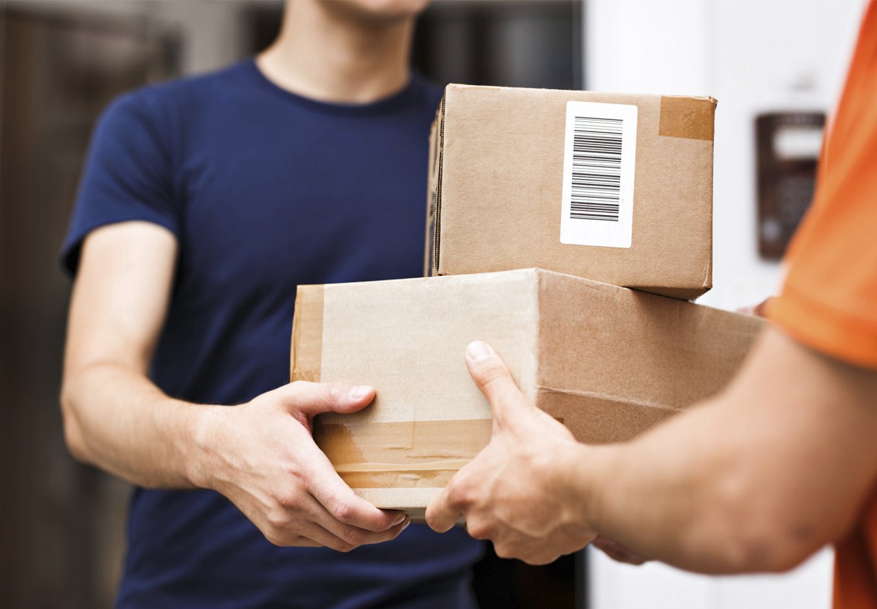 A delivery person handing over two cardboard packages to a customer at the doorway.