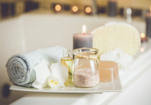 Spa essentials on a tray with a rolled towel, aromatic candles, massage oils, bath salt, and soap.