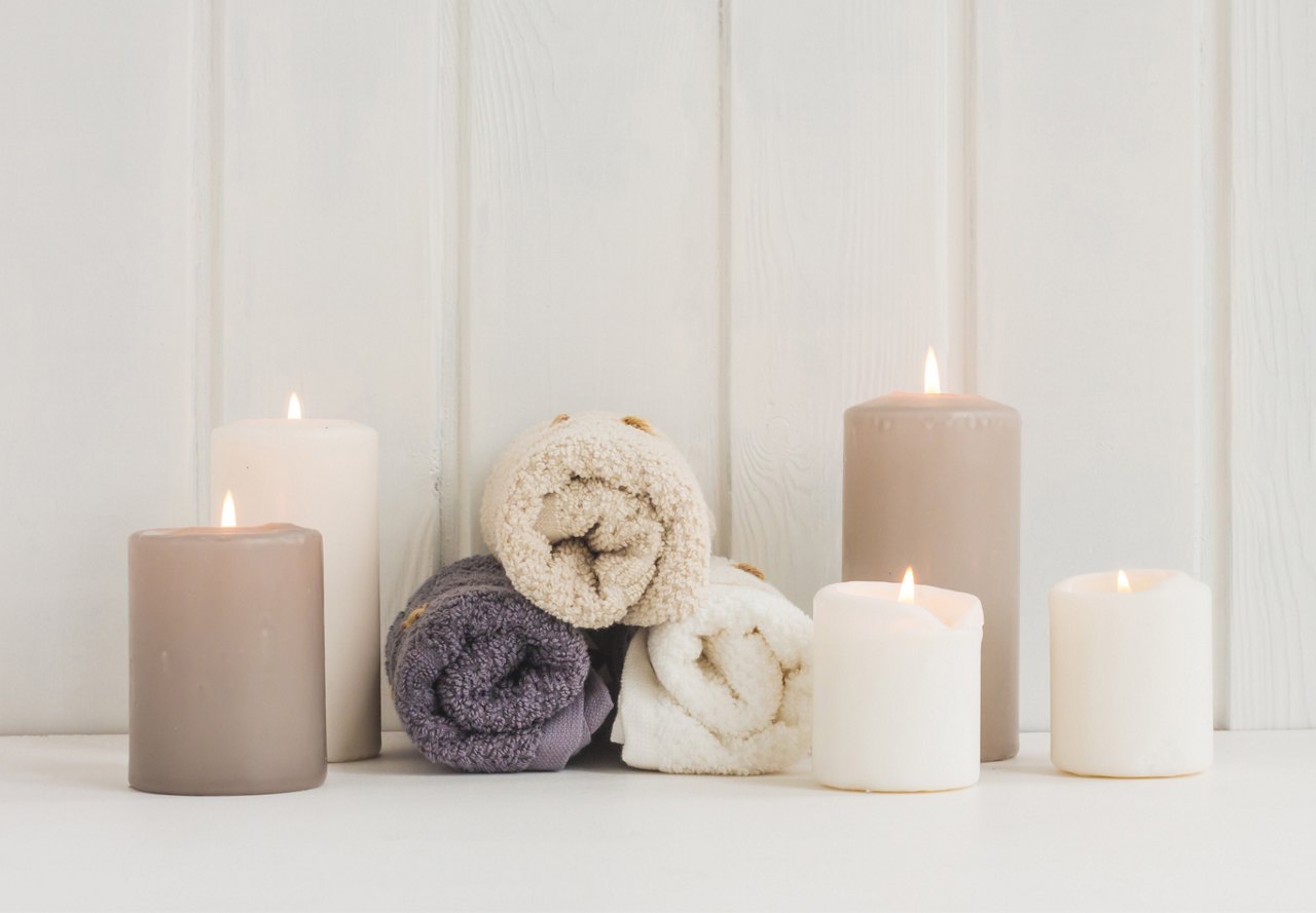 A serene arrangement of lit candles and rolled bath towels on a wooden surface against a white background.