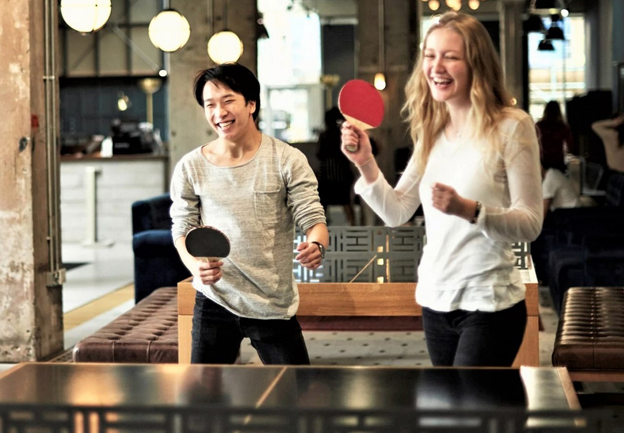 A smiling man and woman playing table tennis in a lively indoor setting with soft lighting.