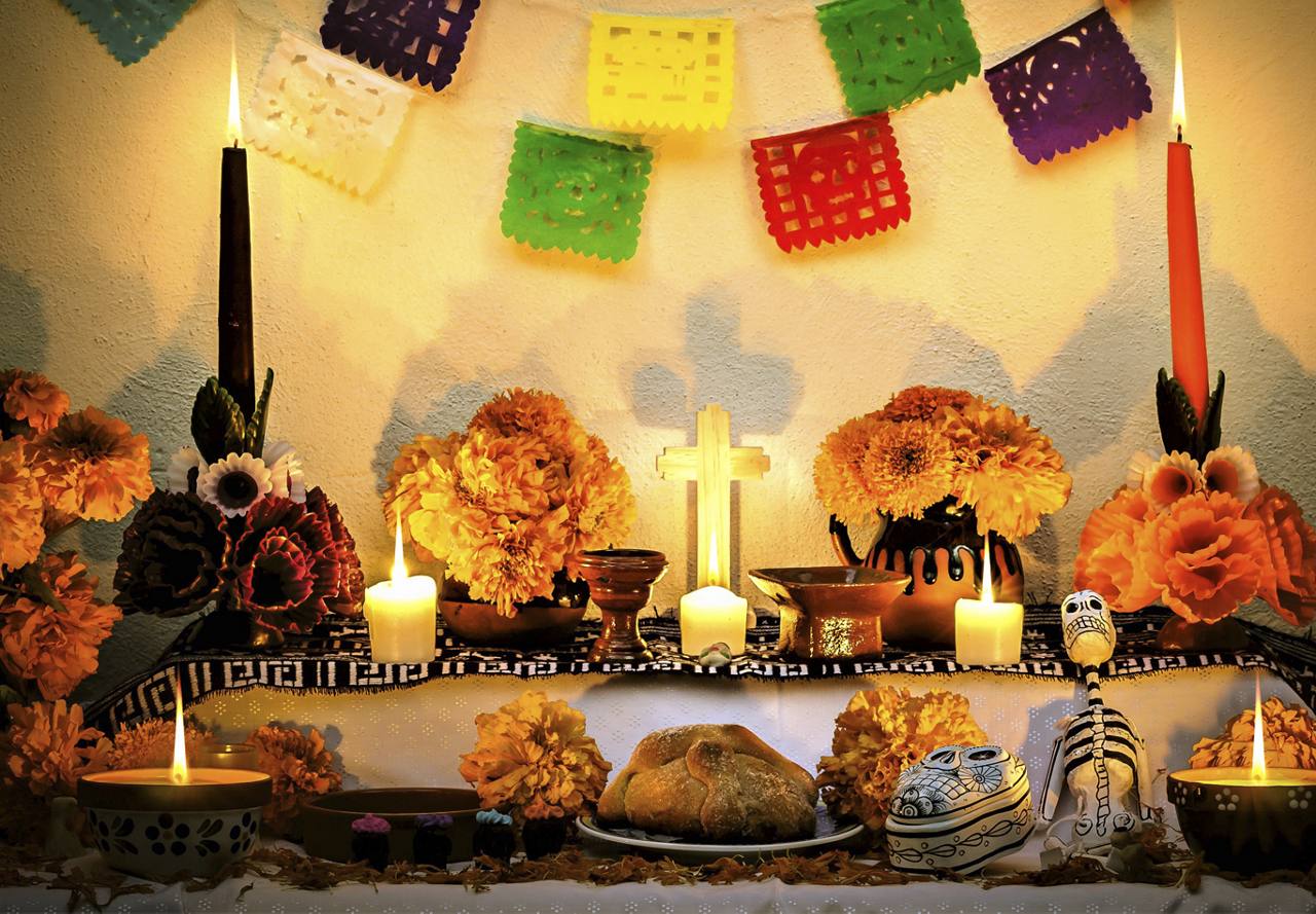 Traditional Day of the Dead altar with candles, marigolds, papel picado, and decorative skulls.