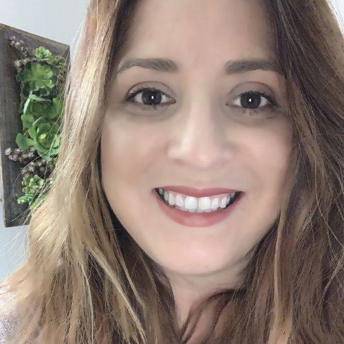 Close-up of a smiling woman with wall-mounted plant decor in the background.