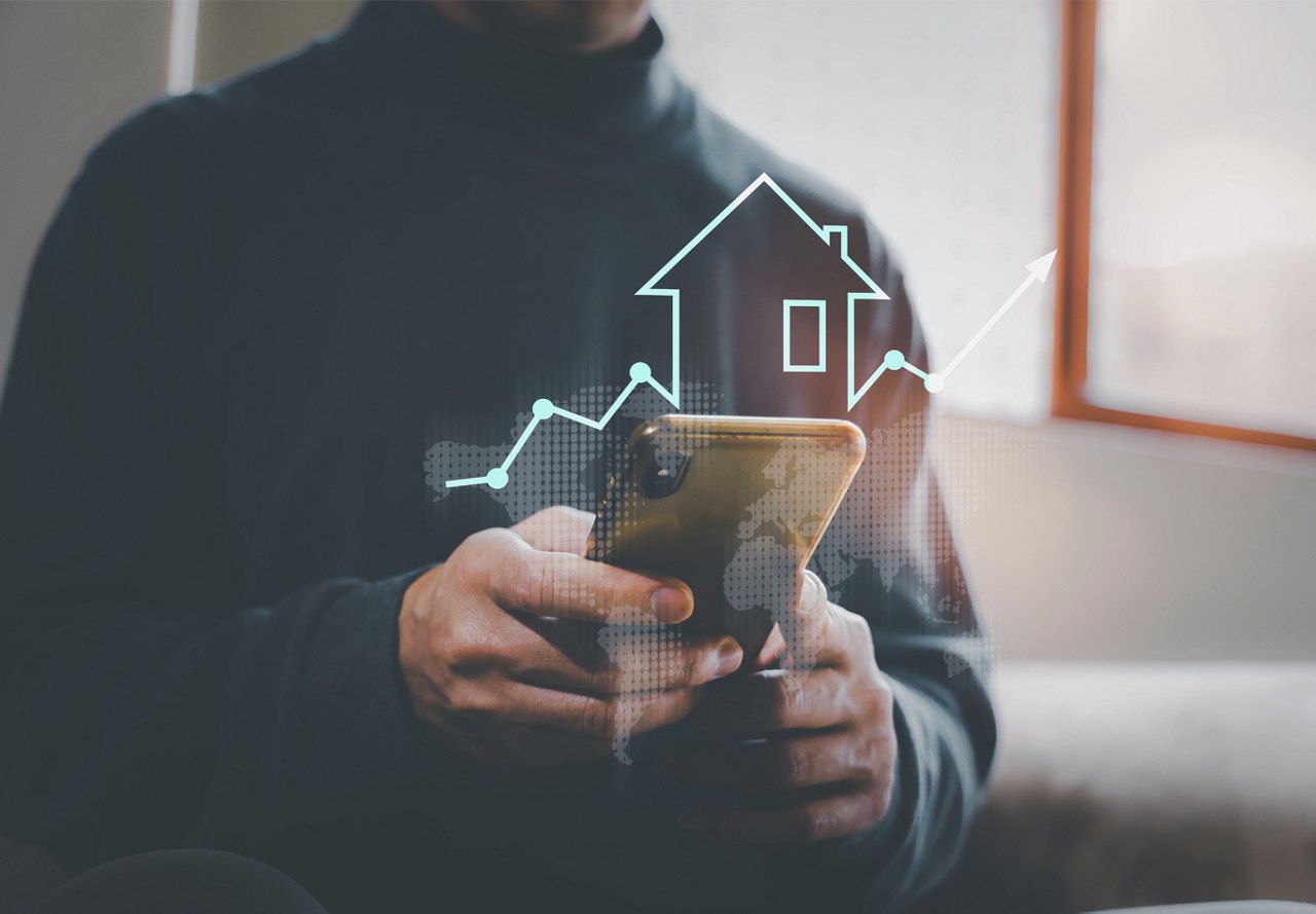 Person in a black turtleneck using a smartphone with a holographic projection of a house and an upward trend graph, depicting real estate analytics.