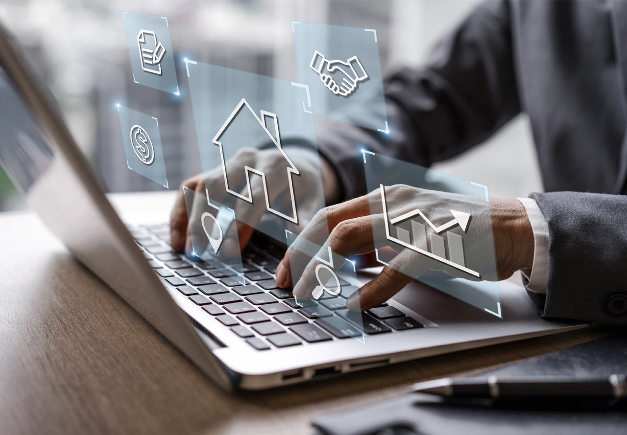 Close-up of hands typing on a laptop with virtual real estate and financial icons floating above the keyboard, indicating online property management.