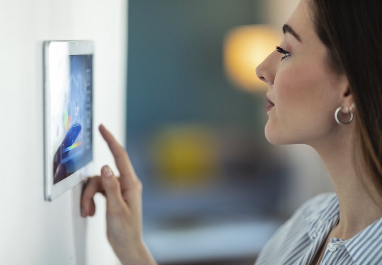 Woman interacting with a smart home control panel on a wall.