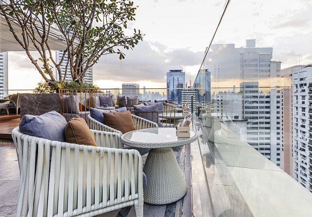 Rooftop terrace with modern furniture and a potted tree overlooking a city skyline at dusk.