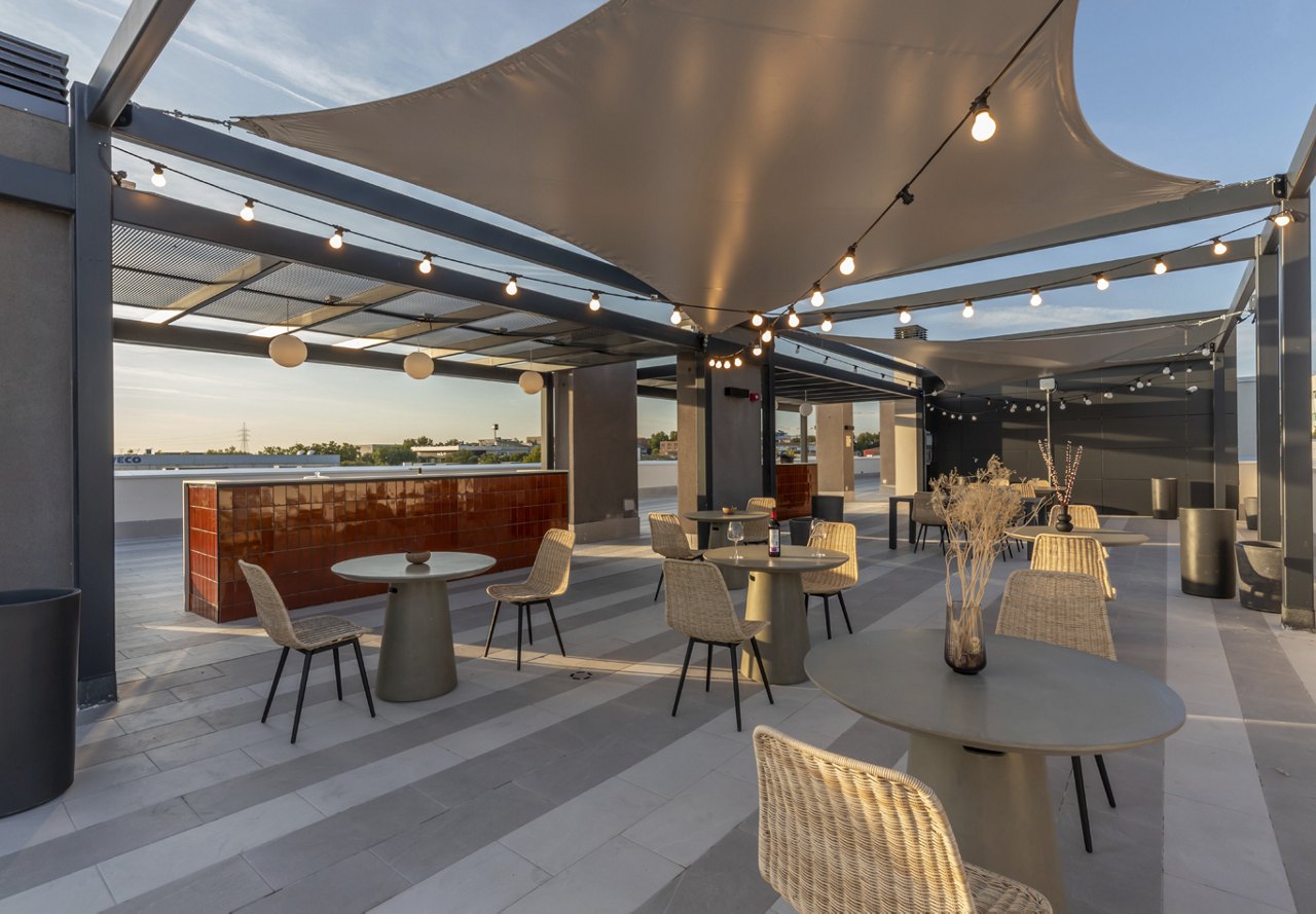 Chic rooftop patio with a bar, shaded seating areas, and string lights against an evening sky.