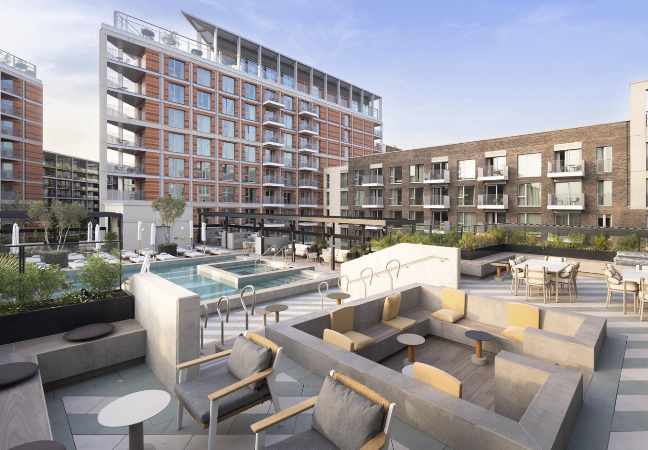 Courtyard-style rooftop with a pool, surrounded by modern apartment buildings, featuring seating and dining areas.