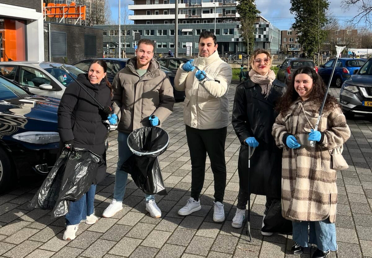 A group of five individuals equipped with gloves and trash bags ready for a community litter cleanup event, standing outdoors with a positive demeanor.