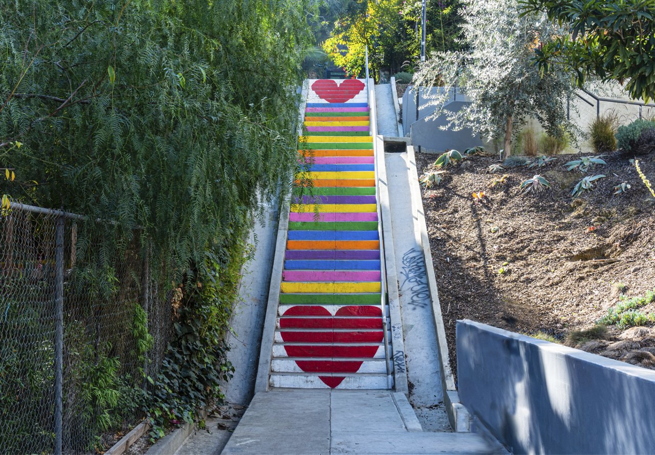 Painted staircase in the Silver Lake neighborhood of California, featuring heart and rainbow designs, surrounded by trees and lush landscape.