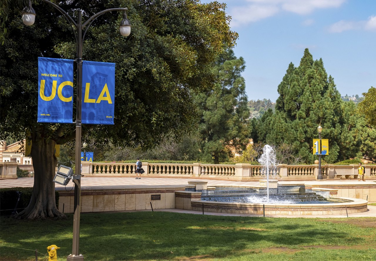 Scenic photo of the UCLA campus in Westwood, featuring a fountain in the background, with trees and students walking to class.