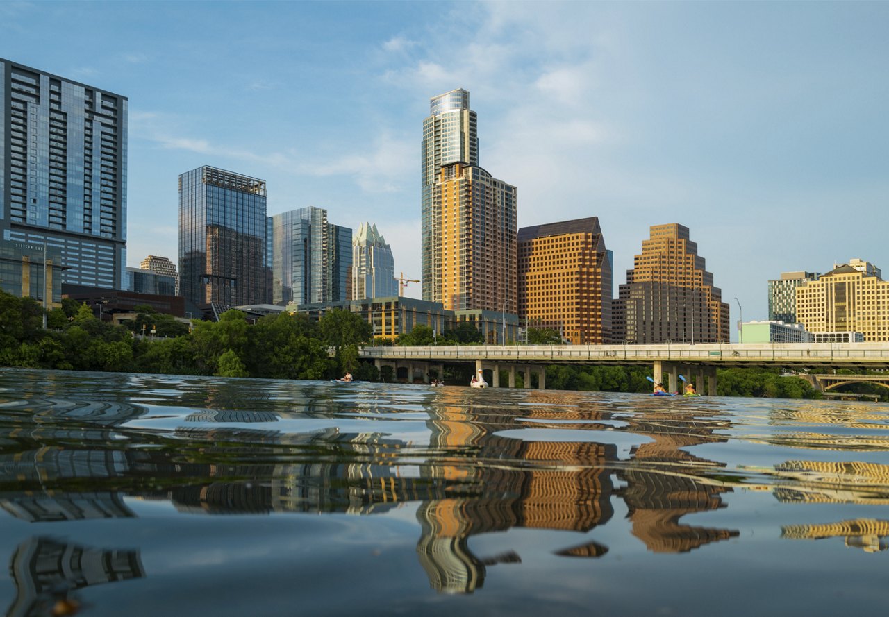 Daytime water-level view of Austin, showcasing the city's sunlit buildings under a clear sky.