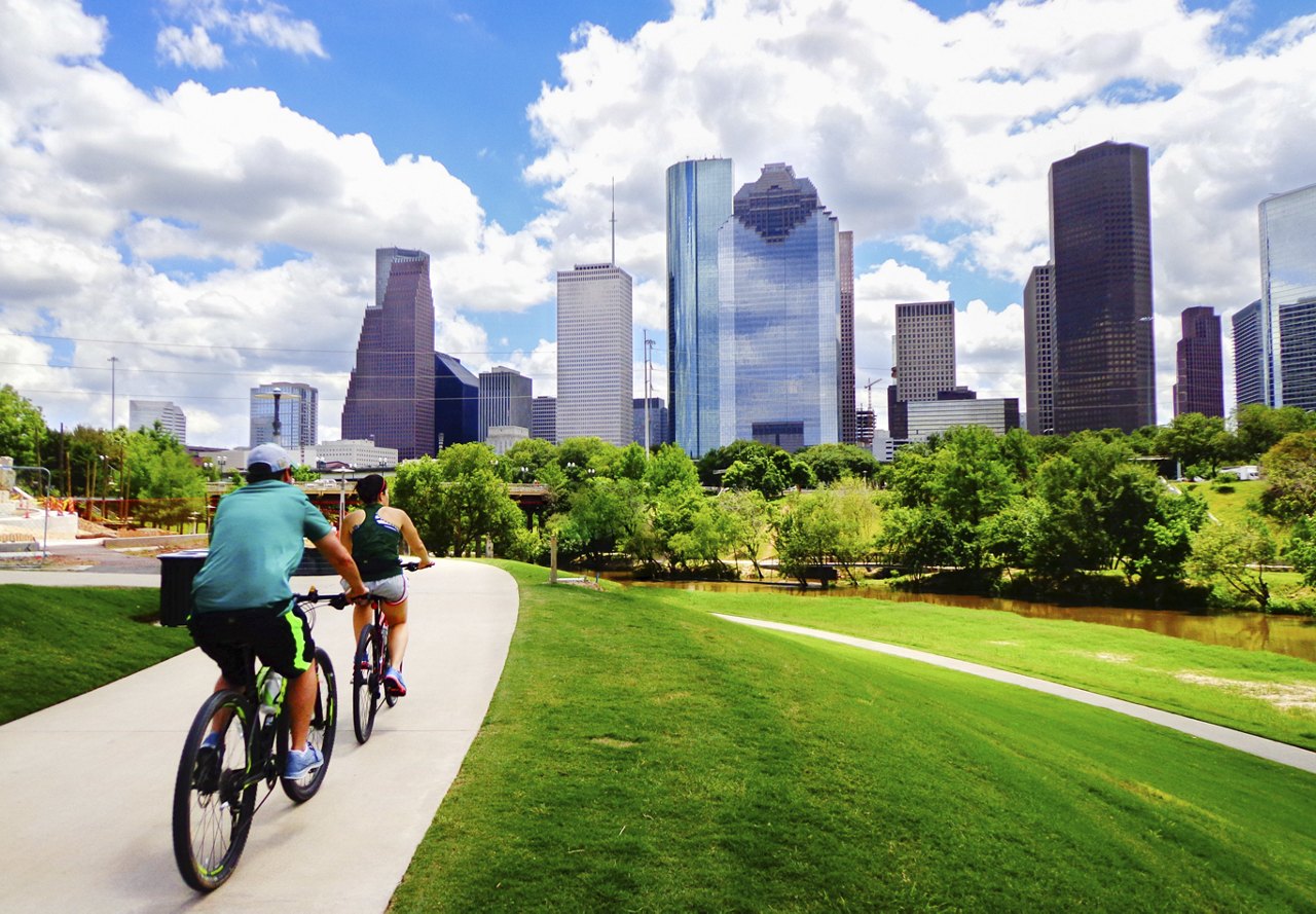 Two residents biking through downtown Houston, enjoying the green spaces and skyline.