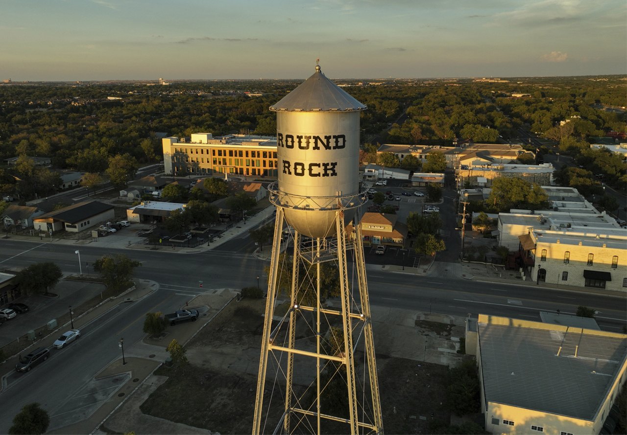 Sunset view of Round Rock, Texas, featuring a water tower with the city's name and various other buildings.