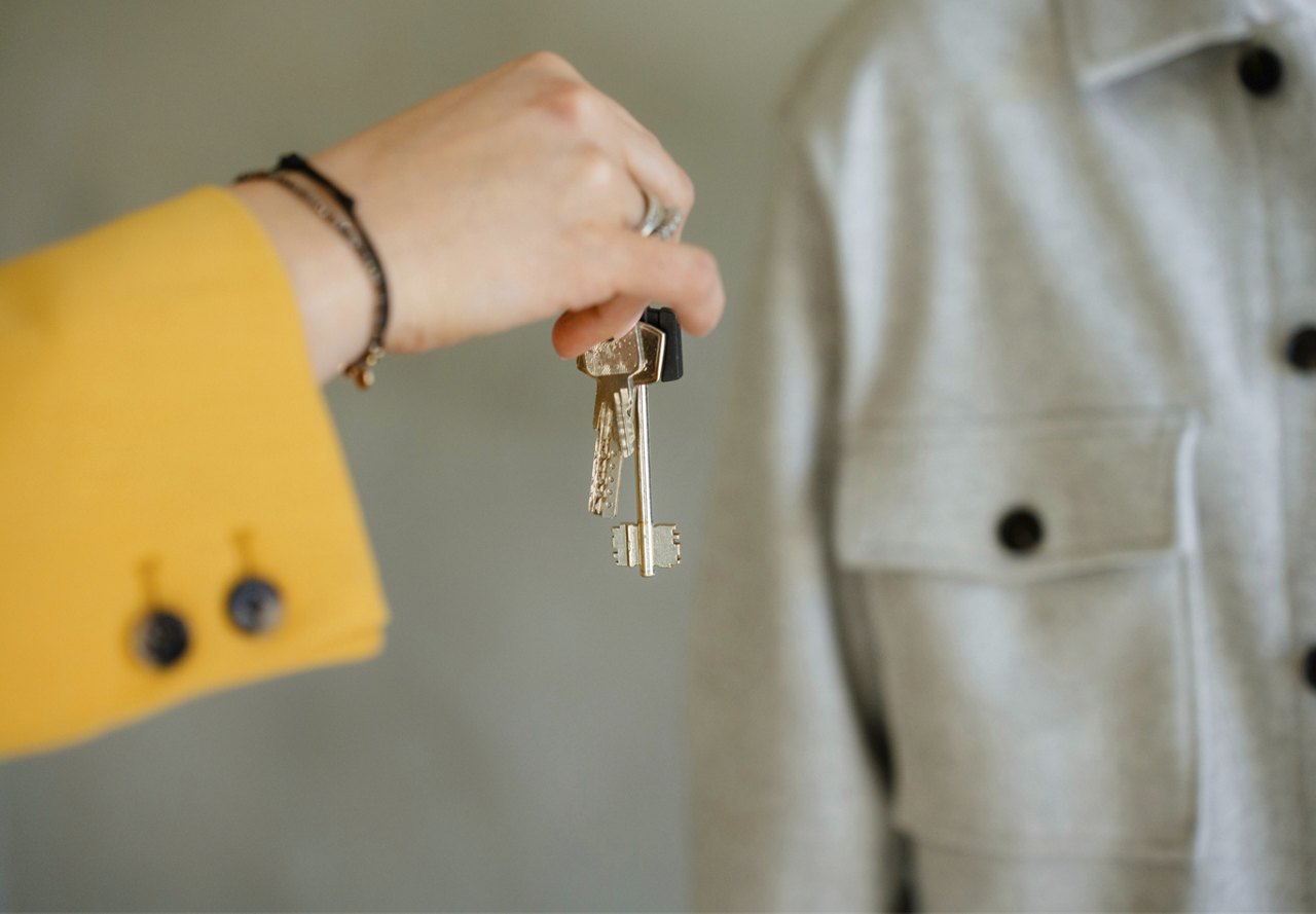 Person in a yellow button-up shirt handing keys to another person wearing a grey shirt.