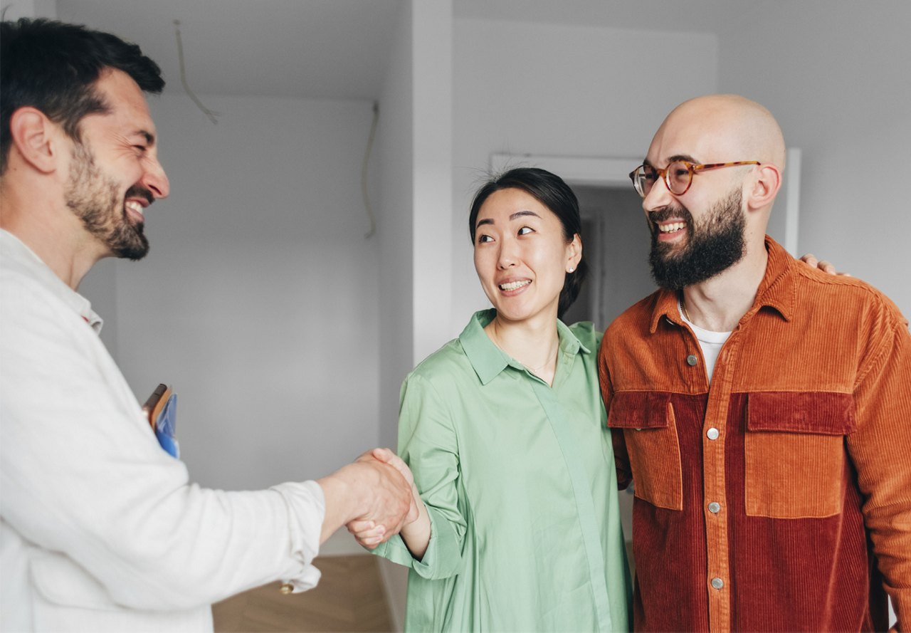 Smiling young couple shaking hands with a real estate agent in a friendly exchange.