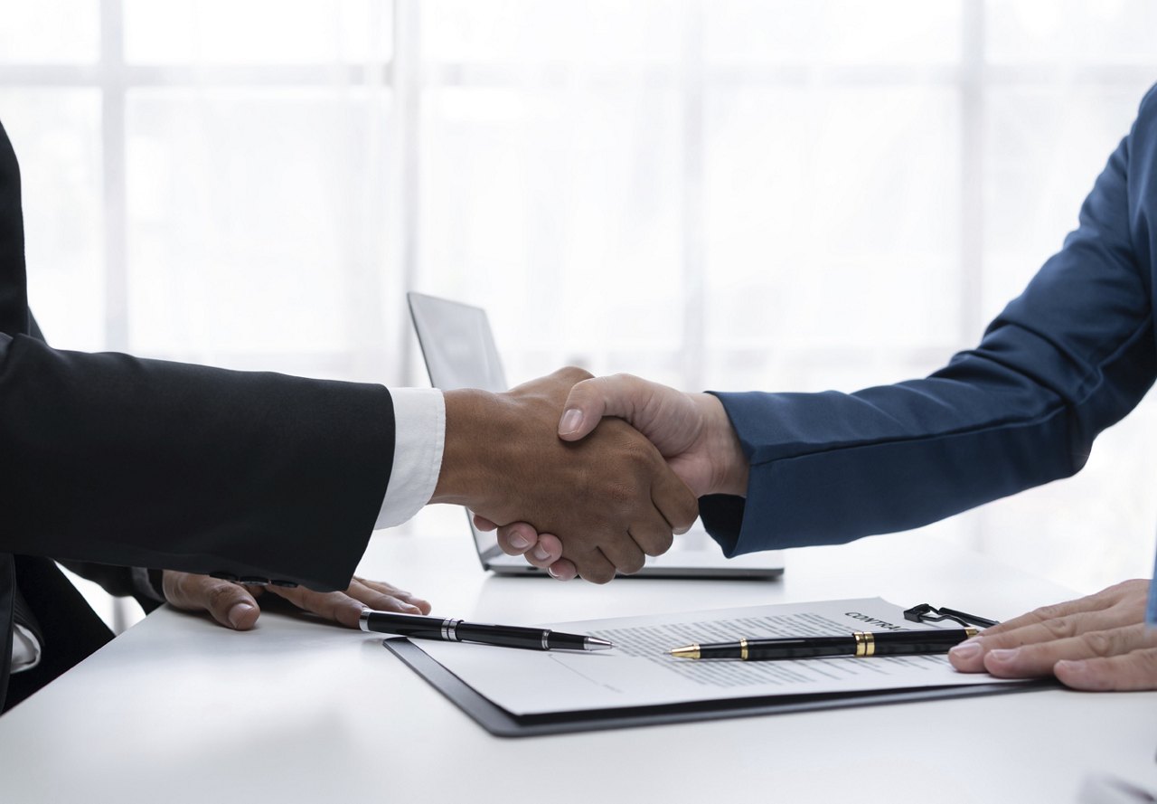 People participating in a business meeting, shaking hands with papers and pens in front of them, where they have just signed an agreement.