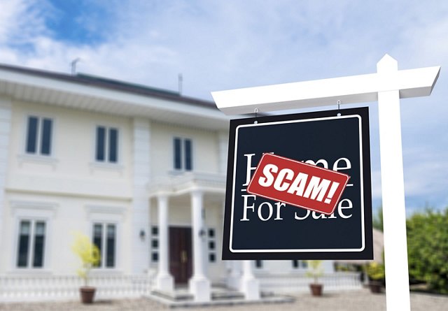 A large house with a sign in the front yard, prominently displaying a 'Scam' sticker over the sign, with the house blurred in the background to focus attention on the sign.