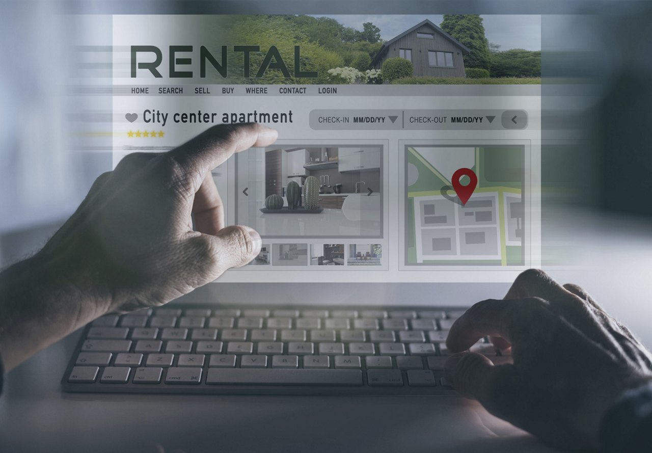 Person pointing at a rental advertisement on the computer screen while typing on the keyboard.