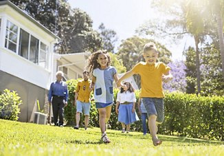 oung children running and enjoying the outdoors in the front yard of their home, with parents and family members watching under the warm, beaming sun.