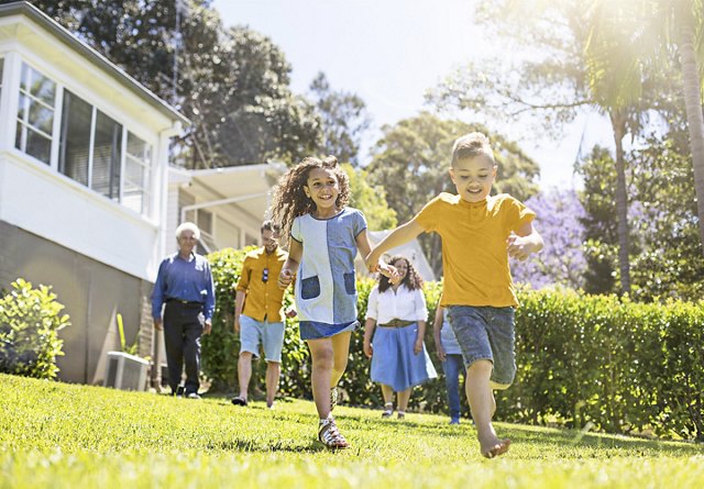 oung children running and enjoying the outdoors in the front yard of their home, with parents and family members watching under the warm, beaming sun.