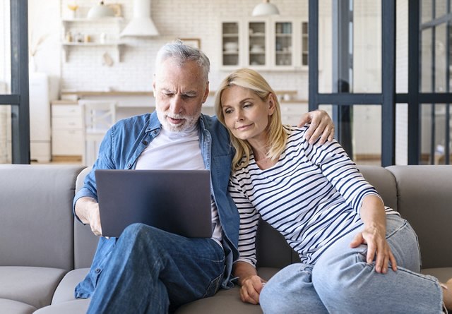 Man and woman sitting on a couch in their modern home, looking at a computer together, with neutral finishes in the surrounding decor.