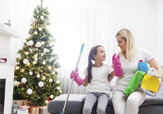 Woman and daughter sitting in their home with cleaning supplies, preparing for the holidays with a Christmas tree in the background.