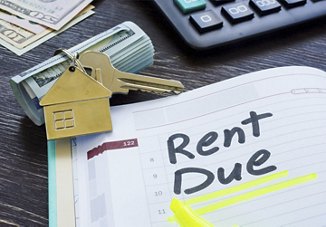 Notebook on a table with 'Rent Due' written on the calendar, a gold key with a house-shaped keychain, a roll of money, and a calculator, all arranged to represent rent payment.