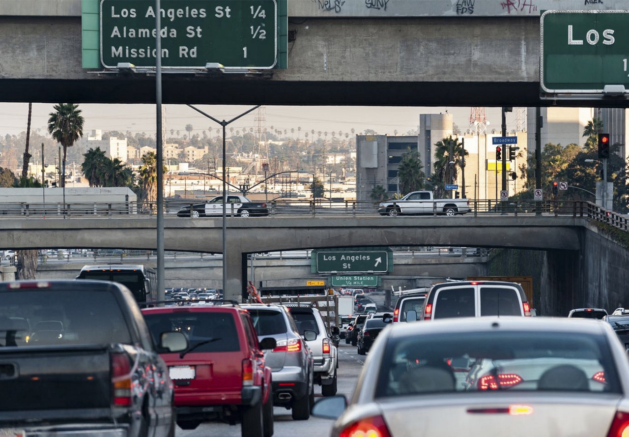 View of traffic on a Los Angeles highway, with overpasses and bridges, and the city skyline in the background.