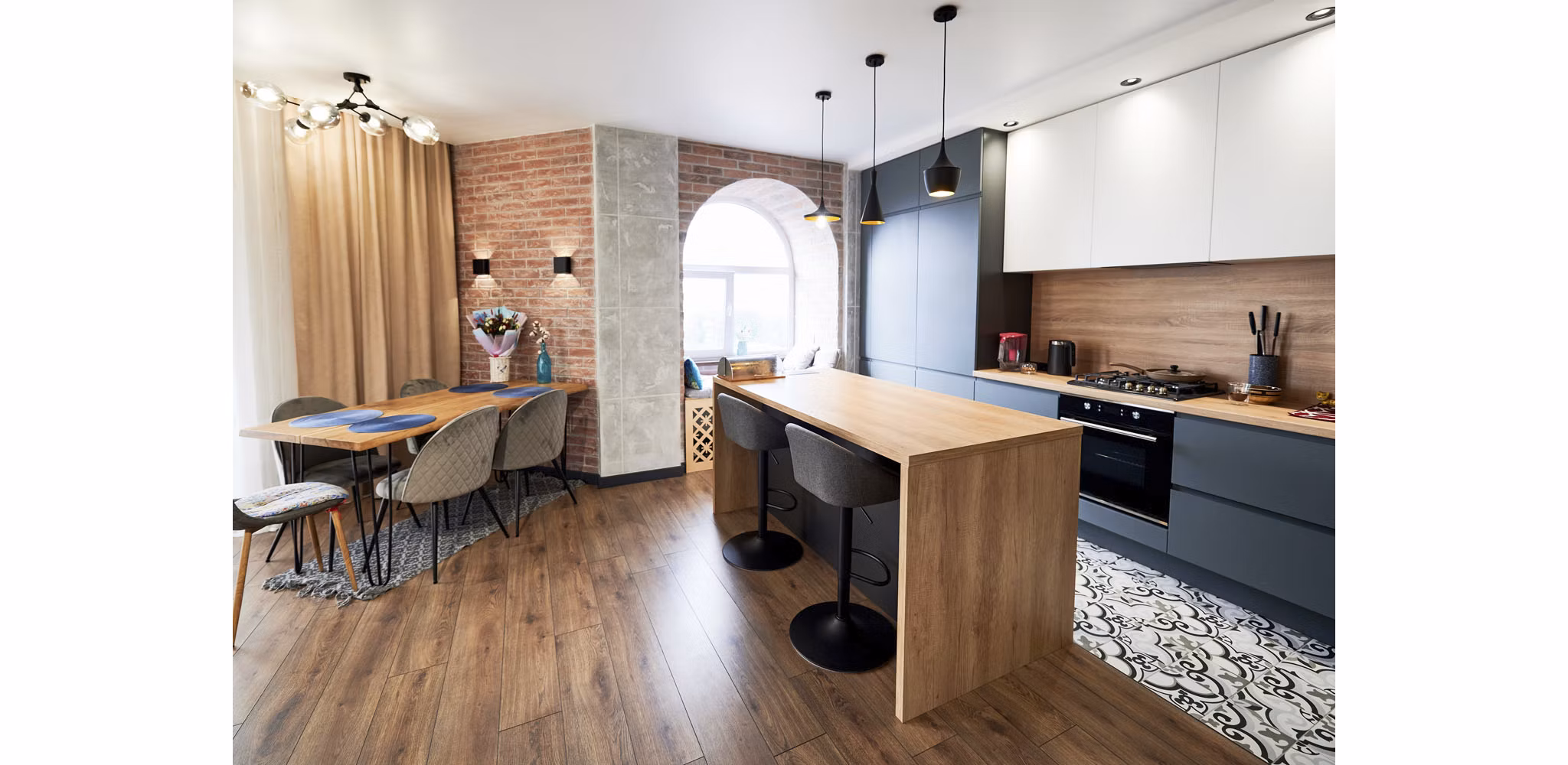 A modern studio apartment featuring brick wall accents, rich wood flooring and paneling, a large round window, and a cozy atmosphere enhanced by sleek, contemporary finishes and touches.