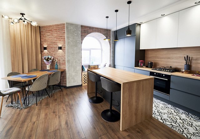 A modern studio apartment featuring brick wall accents, rich wood flooring and paneling, a large round window, and a cozy atmosphere enhanced by sleek, contemporary finishes and touches.