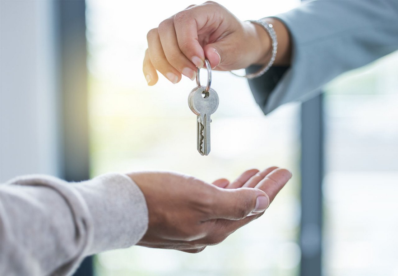 Person receiving a silver key as the resident returns their apartment key after moving out, with a blurred window in the background.