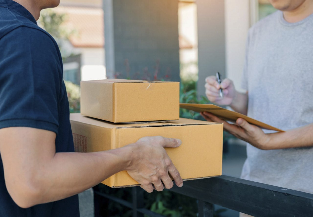 A person delivering packages to a front door, while another individual signs to receive them, with a blurred background focusing on the exchange.