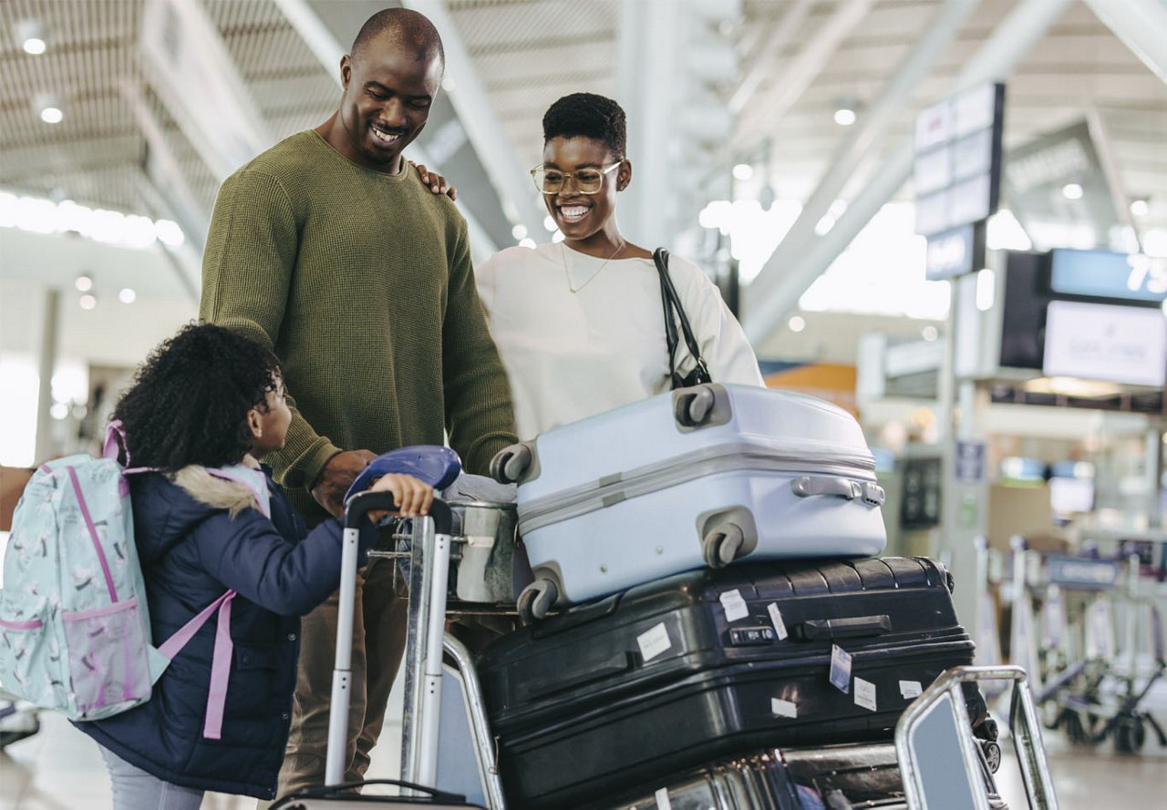 A family at the airport during the holidays, smiling and looking at each other while surrounded by a stack of luggage, preparing to embark on their trip.